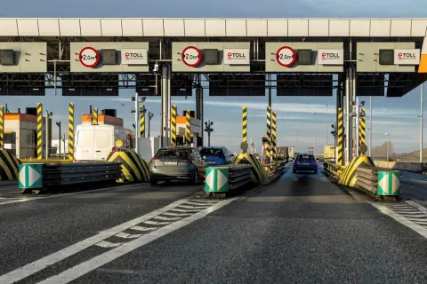 Samochody zbliżają się do bramek poboru opłat za autostrady. Widać znaki eTOLL i ograniczenia wysokości 2,0m.