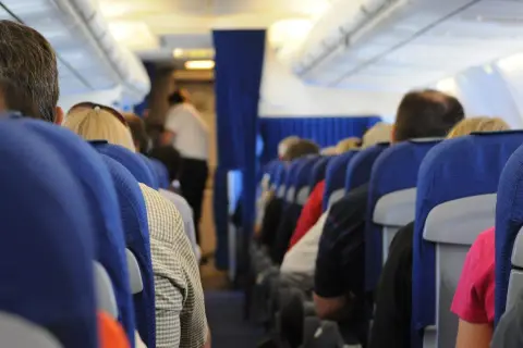 Widok z perspektywy pasażera w samolocie. Siedzący ludzie, niebieskie siedzenia, stewardessa w tle. To może być inspiracja, jak nie bać się latać.
