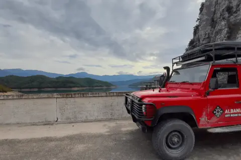 Czerwony Land Rover na tle gór i jeziora w Albanii. Listopad, pogoda pochmurna, idealna na off-road.