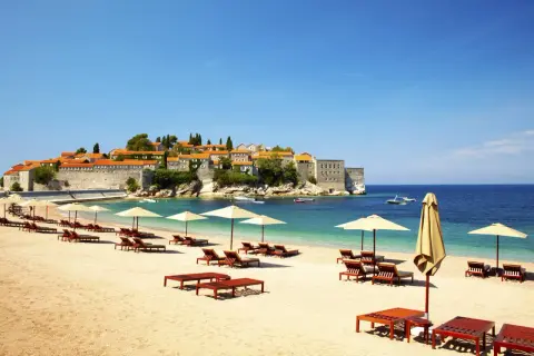 Idealne czarnogóra wakacje all inclusive: piaszczysta plaża, leżaki, parasole i widok na urokliwe miasteczko na wyspie.
