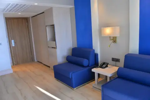Pokój hotelowy z niebieskimi sofami, drewnianymi meblami i drzwiami. Czuć tu **liberty lykia**, wolność i przestrzeń.