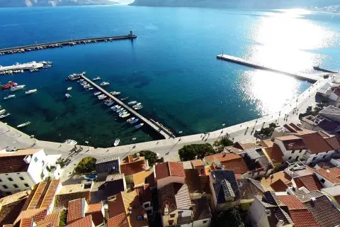 Widok na port i miasteczko Baška w Chorwacji. Woda jest turkusowa, a na nabrzeżu cumują łodzie.