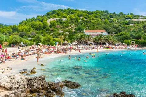 Słoneczna plaża w Chorwacji, ludzie opalają się i kąpią w krystalicznie czystej wodzie. Idealne miejsce na wakacje all inclusive samolotem.
