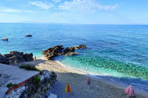 Albania, luty. Słoneczna pogoda nad turkusowym morzem, pusta plaża z leżakami i parasolami, łodzie na wodzie.