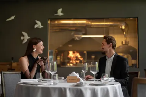 Elegancka para cieszy się romantyczną kolacją w restauracji a la carte all inclusive. Za nimi widać kuchnię z ogniem w piecu.