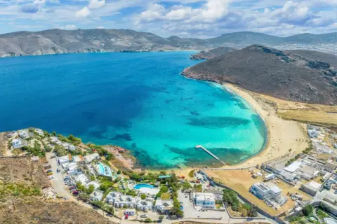 Malownicze Mykonos all inclusive: białe domki, baseny i turkusowa zatoka z piaszczystą plażą.