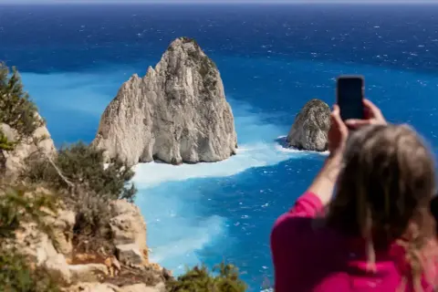 Widok na turkusowe morze Zakynthos, gdzie turystka robi zdjęcie skalistym wysepkom.