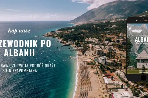 Piękna linia brzegowa Albanii, z widokiem na miasto i góry. Na ekranie telefonu przewodnik po Albanii, idealny na podróż.