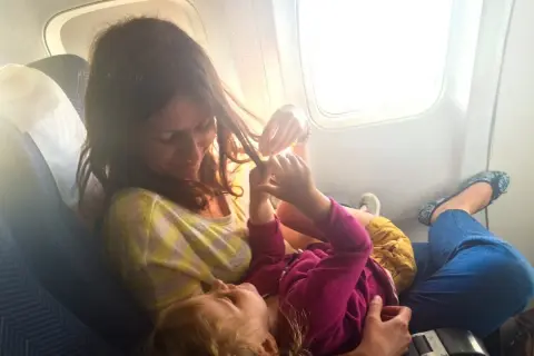 Mama bawi się włosami dziecka w samolocie. Dzieci w samolocie, podróżują z uśmiechem.