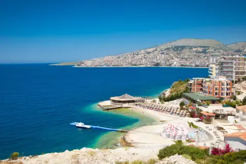 Piękna albania pogoda: błękitne morze, plaża z leżakami i hotelami na wzgórzu.