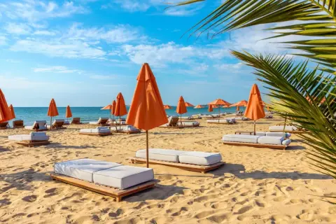 Słoneczny dzień na plaży w Złotych Piaskach. Pomarańczowe parasole i leżaki czekają na gości.