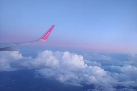 Skrzydło samolotu rejsowego Wizz Air nad chmurami o zachodzie słońca.