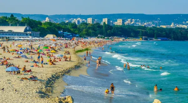 Słoneczna plaża w Bułgarii, idealna na wakacje last minute all inclusive. Tłumy ludzi opalają się i kąpią w morzu.
