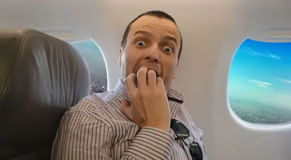 Przerażony mężczyzna w paski, siedzący w samolocie, panicznie boję się latać samolotem. Wpatruje się w okno, gryząc paznokcie.
