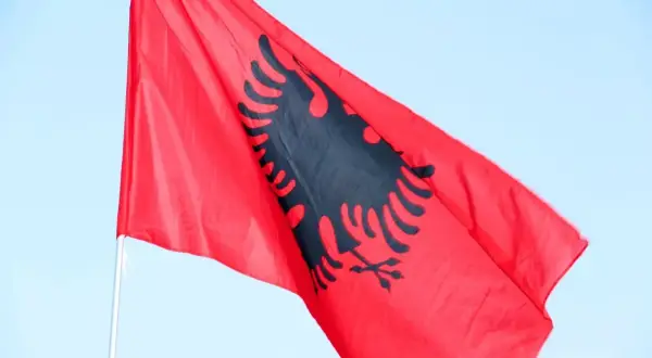 Czerwona flaga Albanii z czarnym dwugłowym orłem powiewa na tle błękitnego nieba. Zastanawiasz się, ile trwa lot do Albanii?