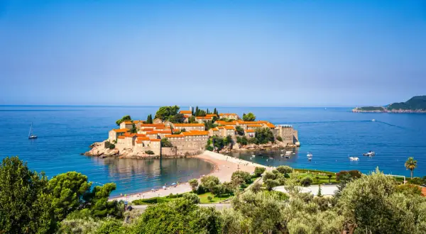 Wyspa Sveti Stefan, jedna z głównych atrakcji Budvy, otoczona turkusowym morzem, z piaszczystą plażą i łodziami.
