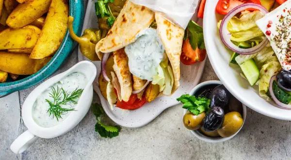 Pyszne dania kuchni greckiej: gyros, sałatka grecka, frytki i sos tzatziki.