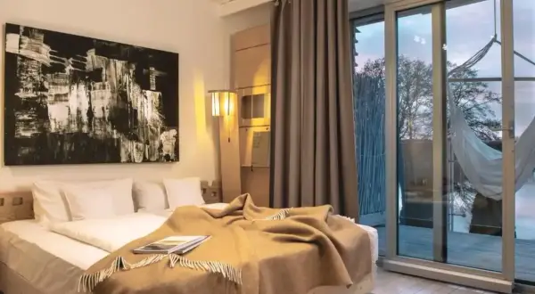 Przytulny pokój w hotelu dla dorosłych z dużym łóżkiem, abstrakcyjnym obrazem i widokiem na jezioro.