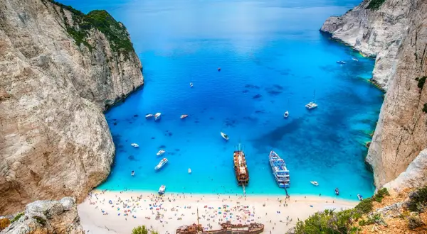 Zatoka Navagio, jedna z największych wysp greckich, z turkusową wodą, plażą pełną ludzi i wrakiem statku.