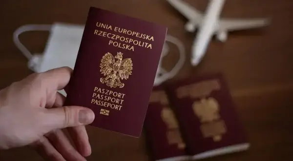 Dłoń trzyma polski paszport. Obok leżą kolejne dokumenty, maseczka i samolot. Zastanawiasz się, ile trwa wyrobienie paszportu?