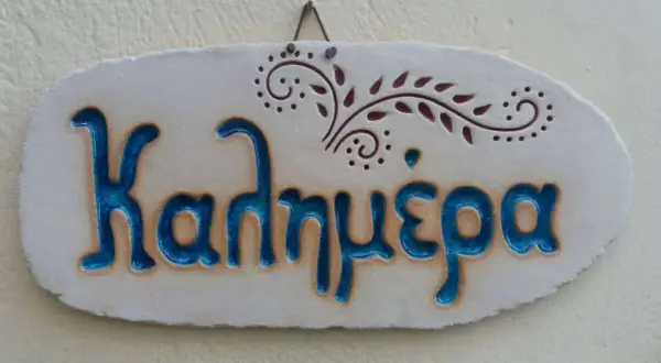 Ceramiczna tabliczka z napisem "Καλημέρα" (do zobaczenia po grecku) i ozdobnym motywem roślinnym.