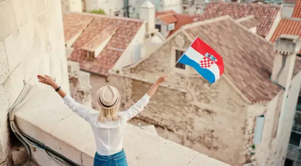 Kobieta z chorwacką flagą na tle dachów. W tle widać piękne, stare miasto.