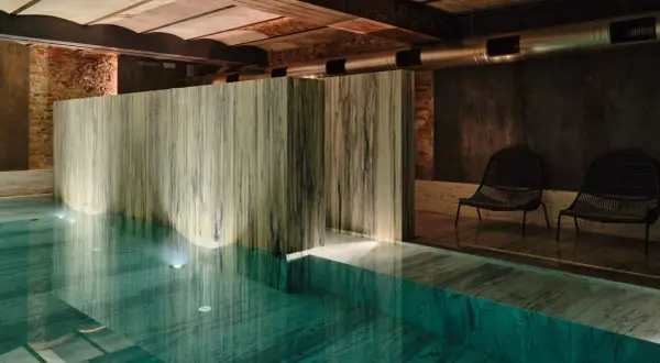 Wnętrze basenu w jednym z najlepszych hoteli spa. Marmurowe wykończenia, dyskretne oświetlenie i dwa fotele tworzą atmosferę relaksu.