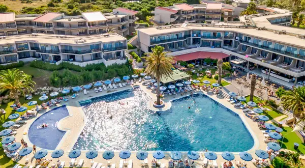 Relaks przy basenie w Cathrin Hotel Rodos. Goście odpoczywają na leżakach pod parasolami, niektórzy pływają w turkusowej wodzie.