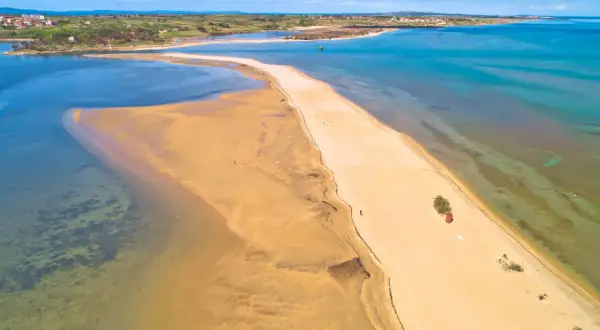 Chorwacja plaże piaszczyste, piaszczysta mierzeja otoczona turkusową wodą, w oddali widać zabudowania.