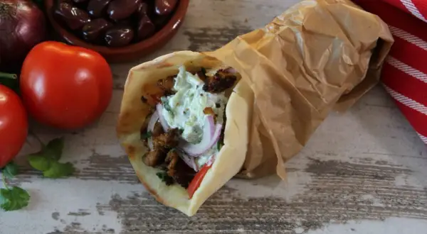 Pyszny pita gyros z mięsem, warzywami i sosem, obok pomidory, oliwki i cebula.