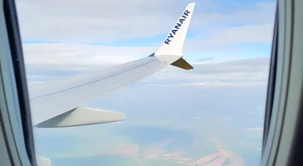 Widok z okna samolotu Ryanair, idealny do nauki, jak szukać tanich wakacji. Podróż nad zielonymi polami i chmurami.