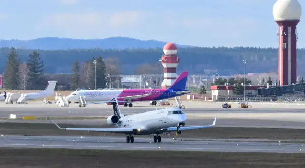 Samolot kołuje po płycie lotniska, gotowy do pierwszego lotu samolotem. W tle różowy samolot Wizz Air i wieża kontroli lotów.