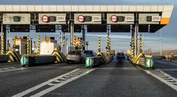 Samochody zbliżają się do bramek poboru opłat za autostrady. Widać znaki eTOLL i ograniczenia wysokości 2,0m.