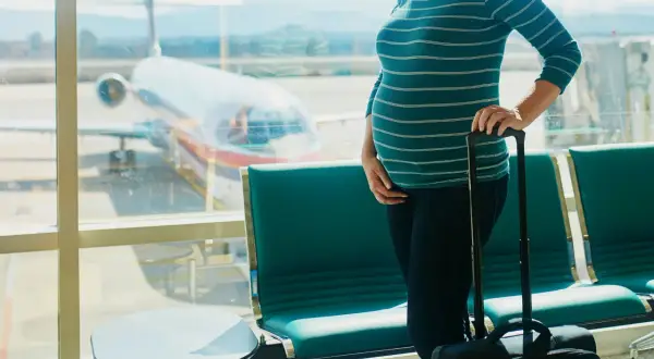 Kobieta w 5 tygodniu ciąży z walizką czeka na lot samolotem w poczekalni lotniskowej.