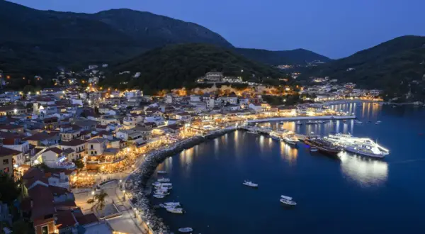 Widok na oświetlone miasto Parga nad morzem o zmierzchu, z górami w tle.