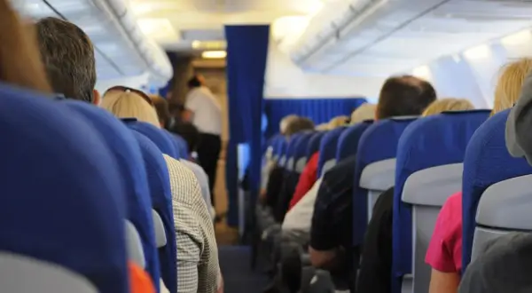 Widok z perspektywy pasażera w samolocie. Siedzący ludzie, niebieskie siedzenia, stewardessa w tle. To może być inspiracja, jak nie bać się latać.