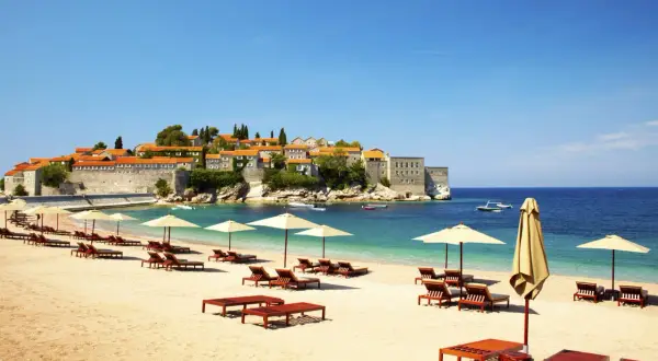 Idealne czarnogóra wakacje all inclusive: piaszczysta plaża, leżaki, parasole i widok na urokliwe miasteczko na wyspie.