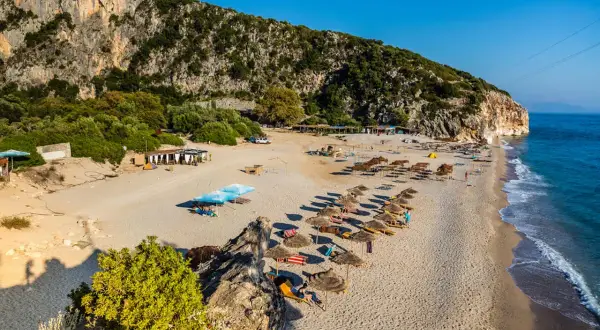 Piękne albania plaże piaszczyste z rzędami parasoli i leżaków, w cieniu skalistego klifu.