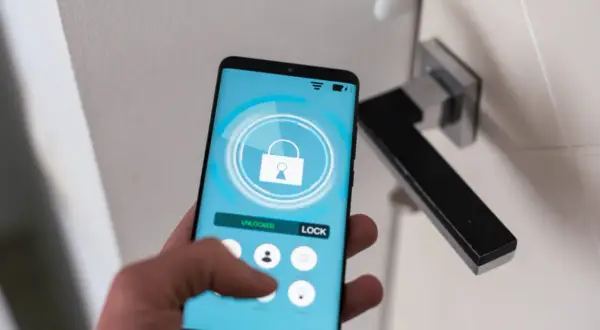 Dłoń trzyma smartfon z aplikacją do zdalnego sterowania zamkiem. Ułatwia to samoobsługowy self check-in.