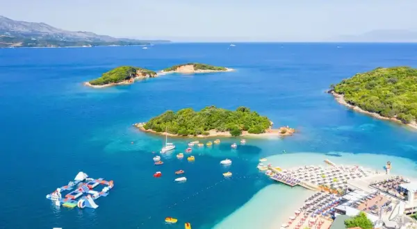 Malownicze **albania morze** z zielonymi wysepkami, plażą z leżakami i wodnym placem zabaw.