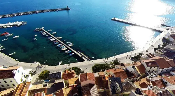 Widok na port i miasteczko Baška w Chorwacji. Woda jest turkusowa, a na nabrzeżu cumują łodzie.