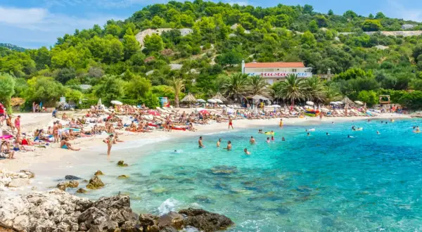 Słoneczna plaża w Chorwacji, ludzie opalają się i kąpią w krystalicznie czystej wodzie. Idealne miejsce na wakacje all inclusive samolotem.