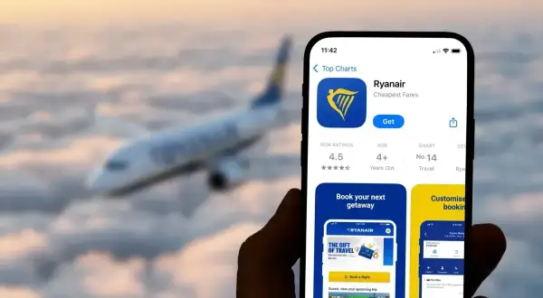 Aplikacja Ryanair na telefonie, z samolotem w tle. Sprawdź, co to za aplikacja do tanich lotów.