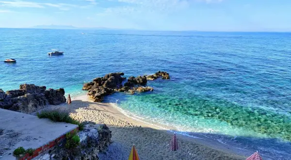 Albania, luty. Słoneczna pogoda nad turkusowym morzem, pusta plaża z leżakami i parasolami, łodzie na wodzie.