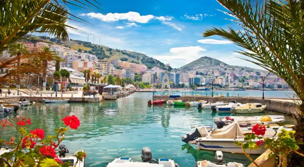Albania, lipiec: słoneczna pogoda nad zatoką z łodziami i palmami. Miasto na wzgórzu w tle.