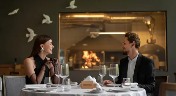 Elegancka para cieszy się romantyczną kolacją w restauracji a la carte all inclusive. Za nimi widać kuchnię z ogniem w piecu.