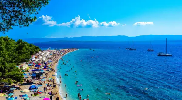 Wyspa Brać oferuje niezapomniane atrakcje: plaża Zlatni Rat tętni życiem, ludzie kąpią się w turkusowej wodzie, a żaglówki kołyszą się na morzu.