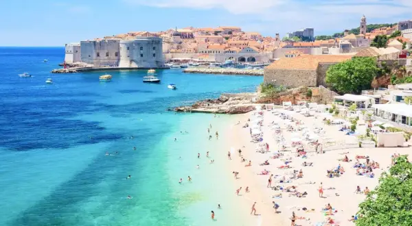 Słoneczna plaża w Dubrowniku, idealna na chorwacja last minute all inclusive. Turkusowe morze, zabytkowe mury i mnóstwo wypoczywających.