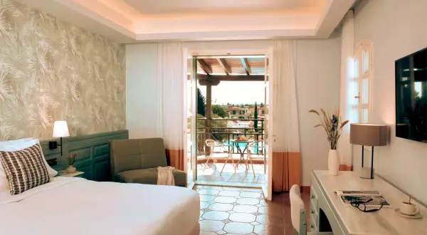Pokój w Eretria Hotel & Spa Resort z widokiem na basen i morze. Wygodne łóżko, fotel i balkon zapraszają do relaksu.
