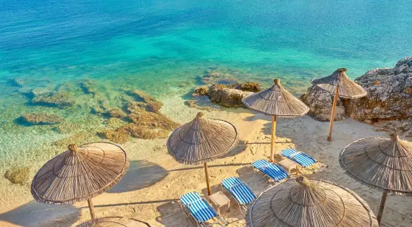 Słoneczna plaża w Ksamilu, Albania. Leżaki pod strzechą czekają na gości pakietu all inclusive.